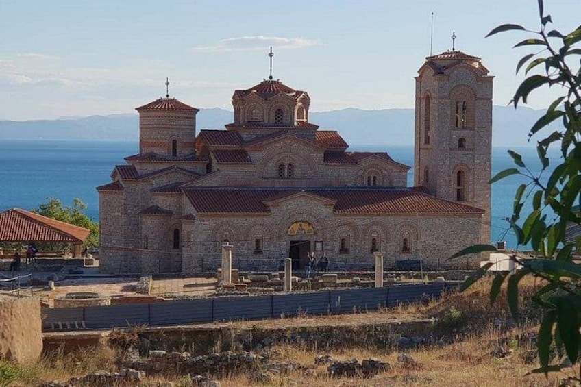 Una iglesia de piedra con dos torres, una entrada arqueada grande y vista al mar de fondo. 1