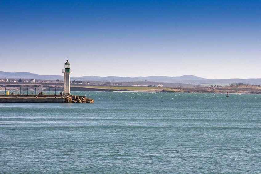 A lighthouse on a pier, calm water, and distant hills. 2