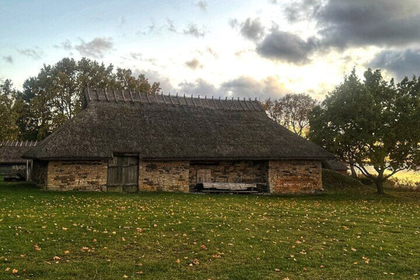 A stone building with a thatched roof, surrounded by a grassy field with scattered yellow flowers. 5