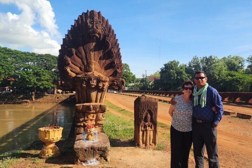 A large stone sculpture by a river, a small bridge, and lush greenery in the background. 1