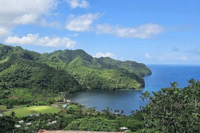 A coastal landscape with lush green hills, a calm sea, and a small settlement with houses. 1