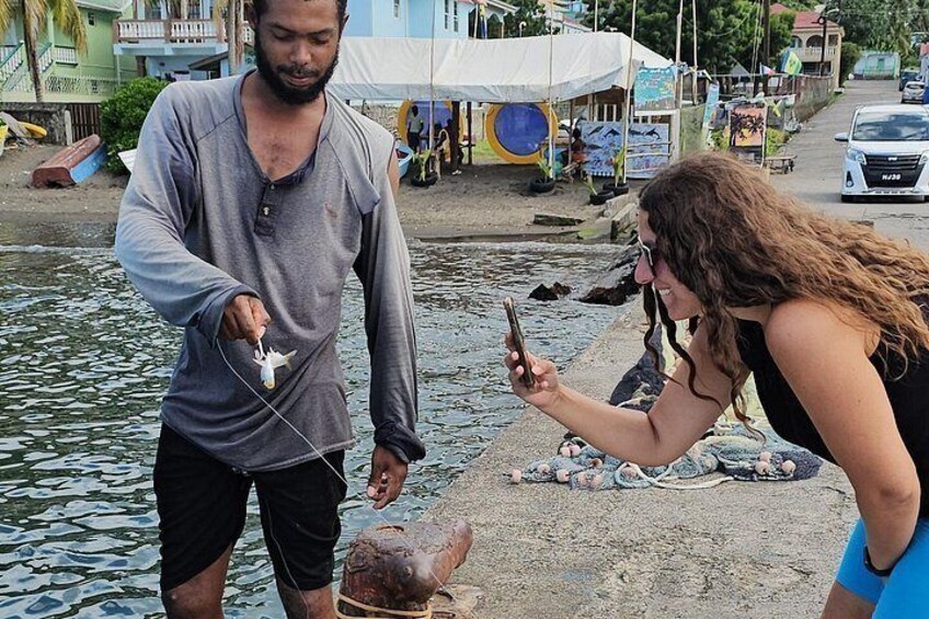 A person holding a fish, another person taking a photo, and a boat in the background. 4