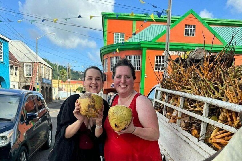 Two people holding coconuts in front of a colorful building with a green roof. 2