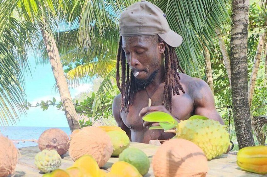 A person with dreadlocks on a beach surrounded by various fruits. 5