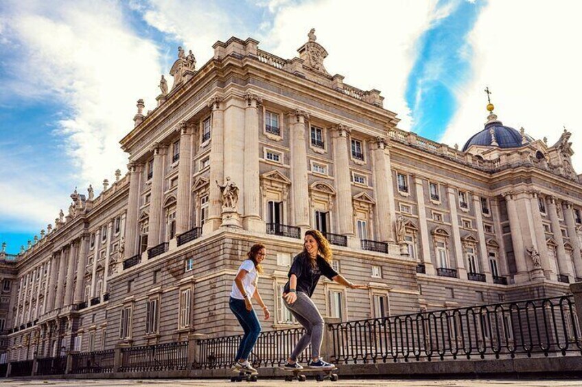 Two people skateboarding in front of a large historic building with ornate architecture. 1