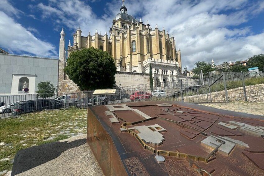 A large historical building with a prominent bell tower, surrounded by a fenced area with a metal roof. 2