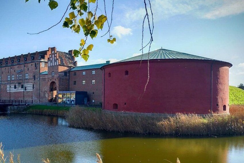 A red cylindrical building near a water body with a brick structure in the background. 3