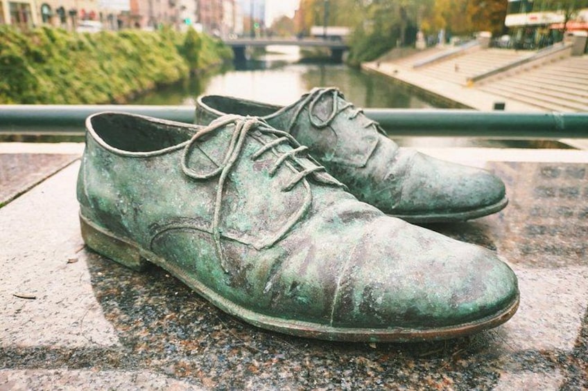 A pair of worn green shoes on a stone surface with a river and bridge in the background. 5