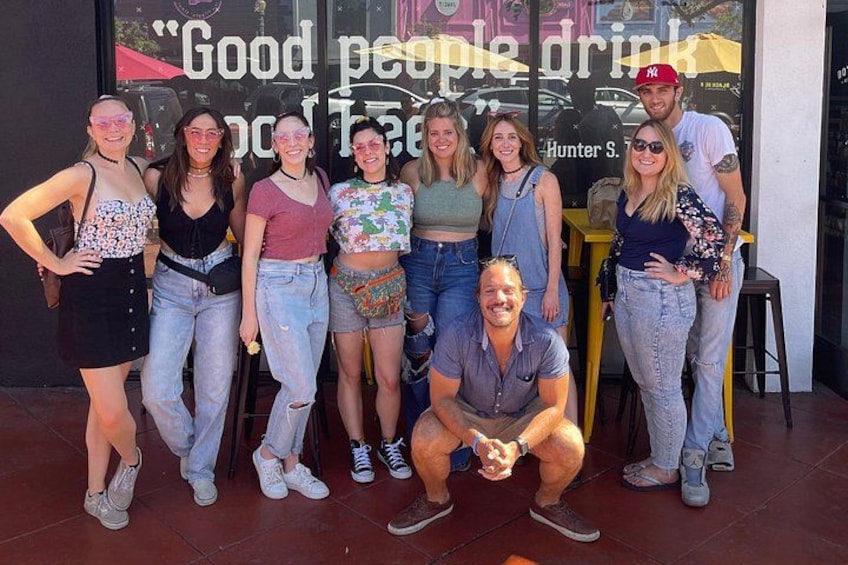 A group of people posing in front of a storefront with a sign that reads 'Good people drink.' 3