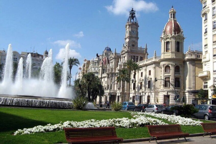 A fountain, a building with a clock tower, and a park with benches. 3