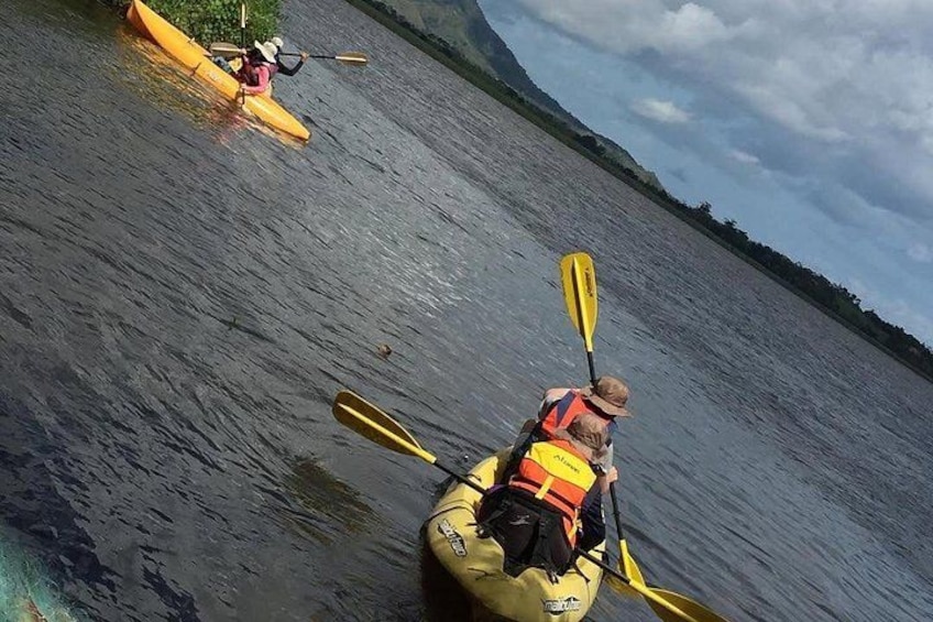 Two kayakers on a calm river, one in a yellow kayak and the other in a red kayak, both wearing life jackets. 5