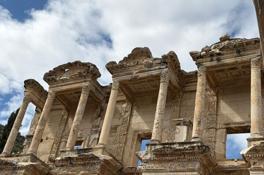 Ancient ruins with columns and intricate carvings against a partly cloudy sky. 4
