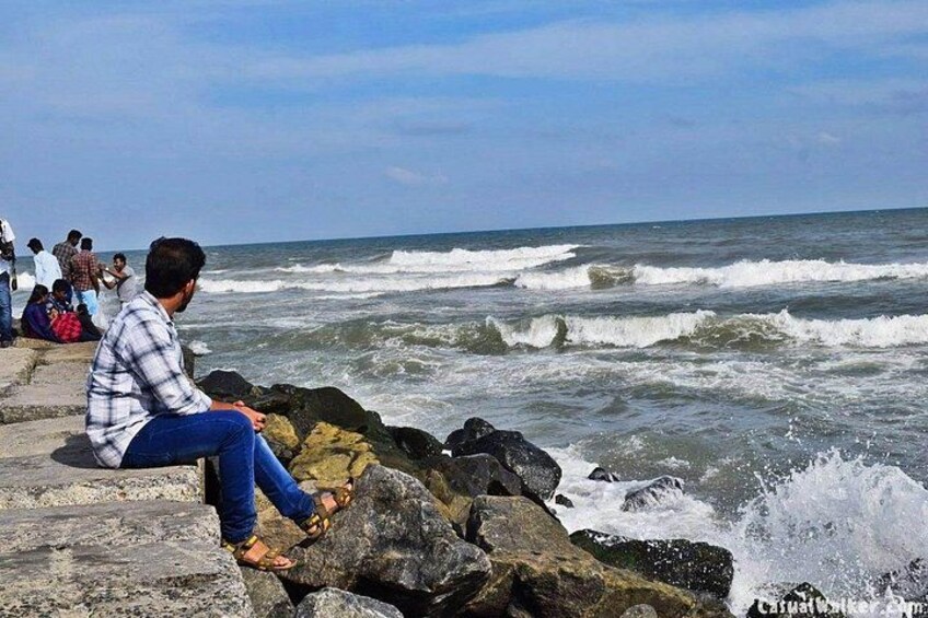 A person sitting on rocks by the ocean, waves crashing nearby. 1
