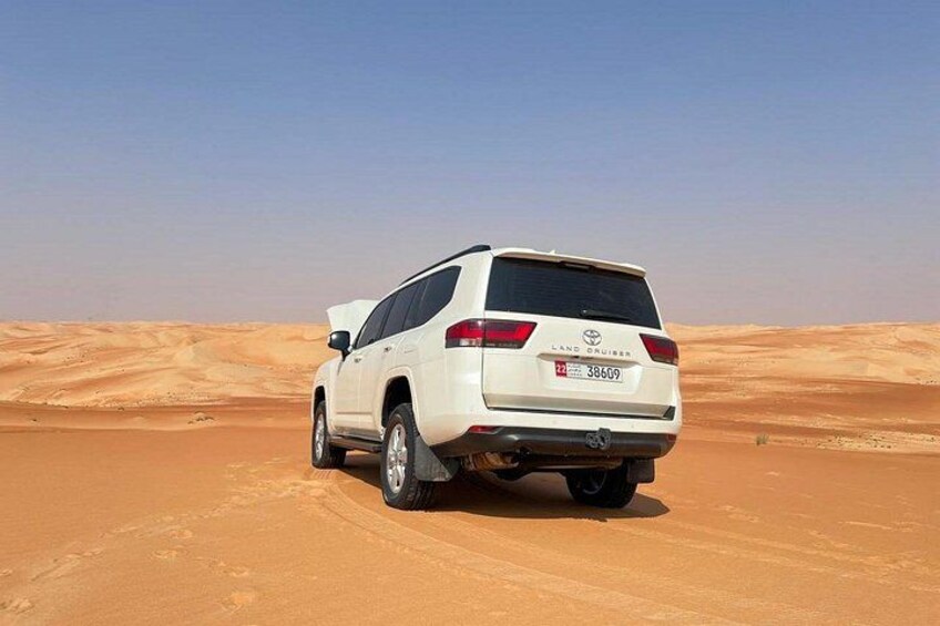 Un SUV blanco aparcado en un desierto con dunas de arena al fondo. 3
