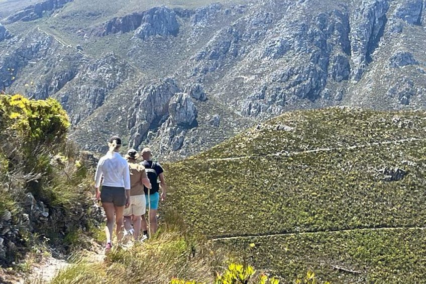 A group of people hiking on a mountain trail with rocky terrain and sparse vegetation. 3