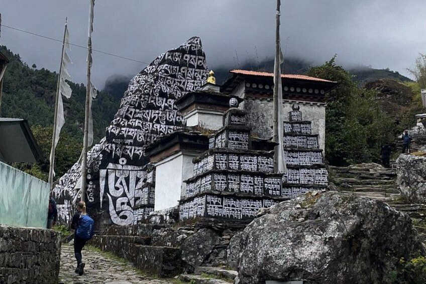 A stone structure with inscriptions, a person walking, and a mountainous landscape. 2