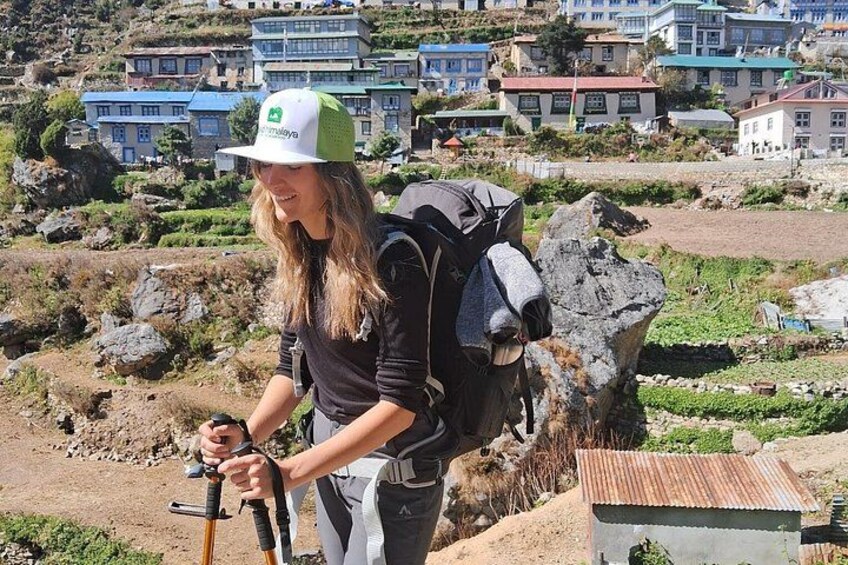 A person hiking with a backpack and a walking stick, surrounded by rocky terrain and houses in the background. 5
