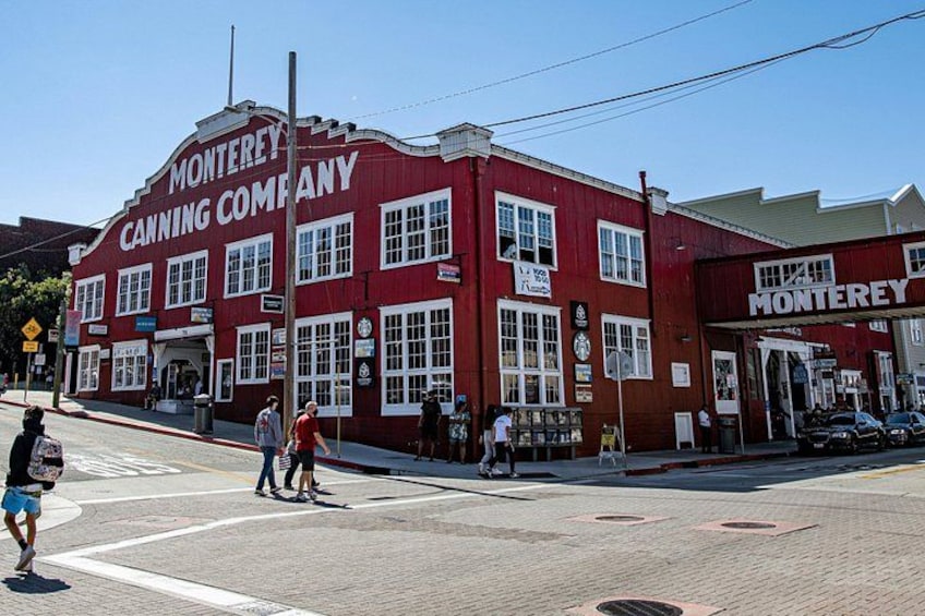 Un edificio rojo con letrero de 'Monterey Canning Company', un paso de peatones y algunas personas caminando. 1