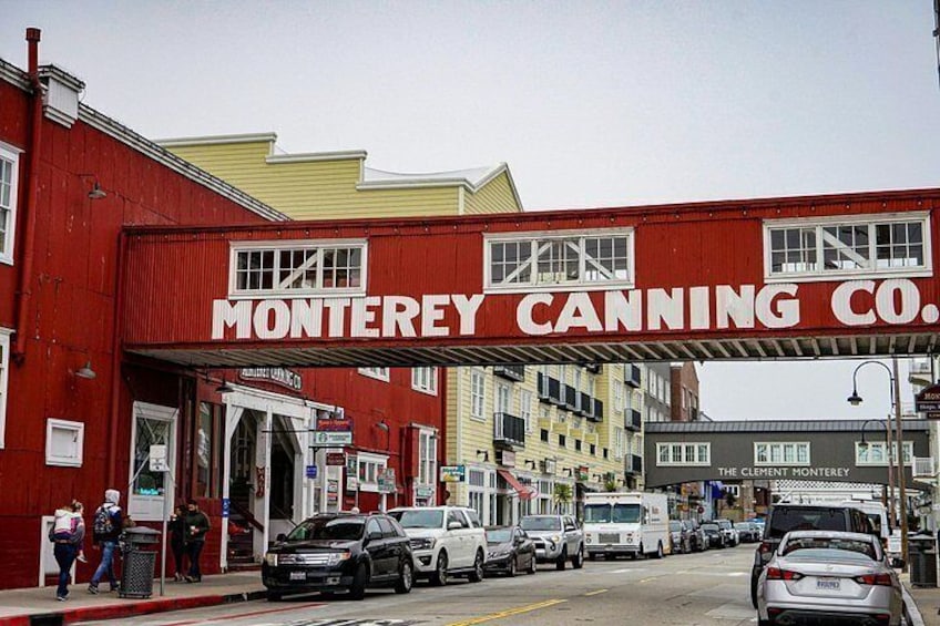 Una calle con un edificio rojo identificado como 'Monterey Canning Co.' y automóviles estacionados. 3