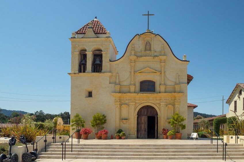 Una iglesia con un campanario, escalones que conducen a la entrada y plantas en macetas al frente. 2