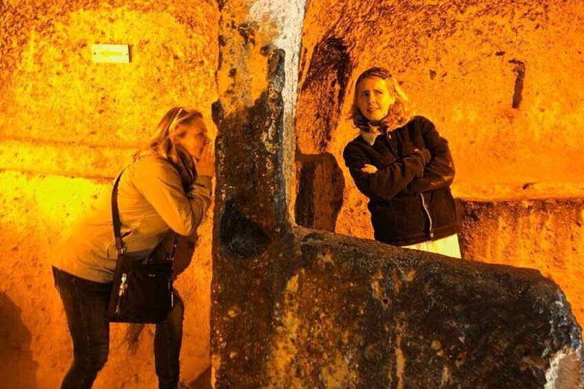 Two people standing in a cave with rough, textured walls. 4