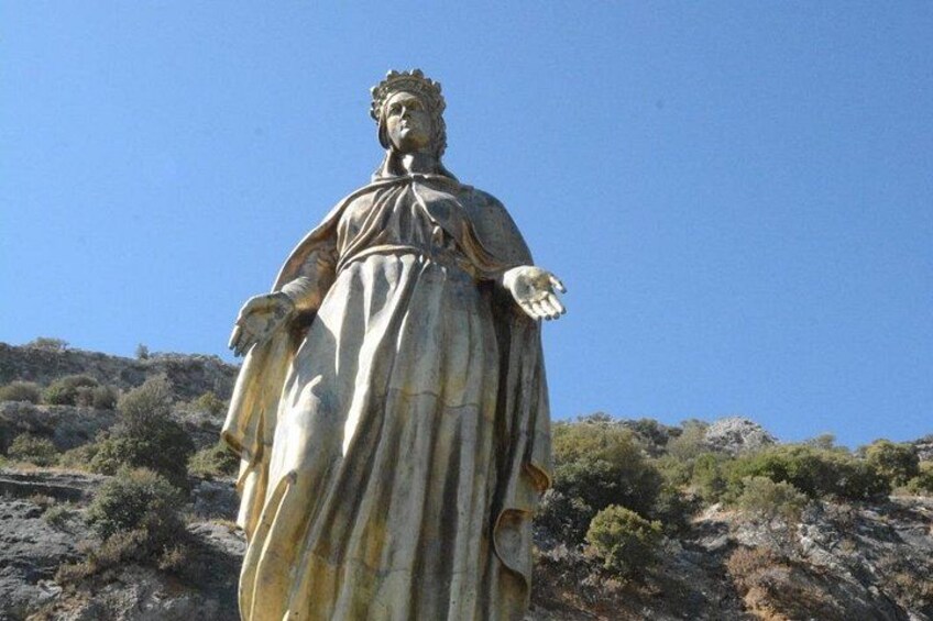 A statue of a robed figure with a halo, standing on a hill with sparse vegetation. 4