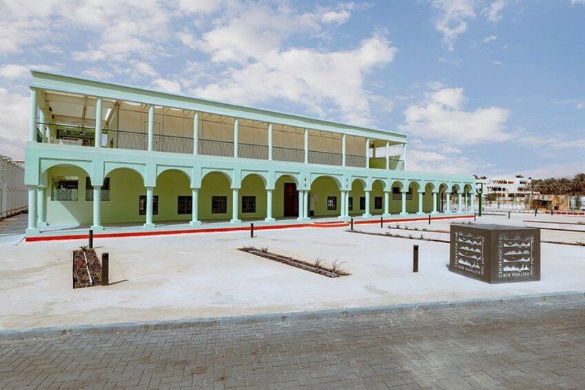 A light green building with a covered walkway and arched openings. 1