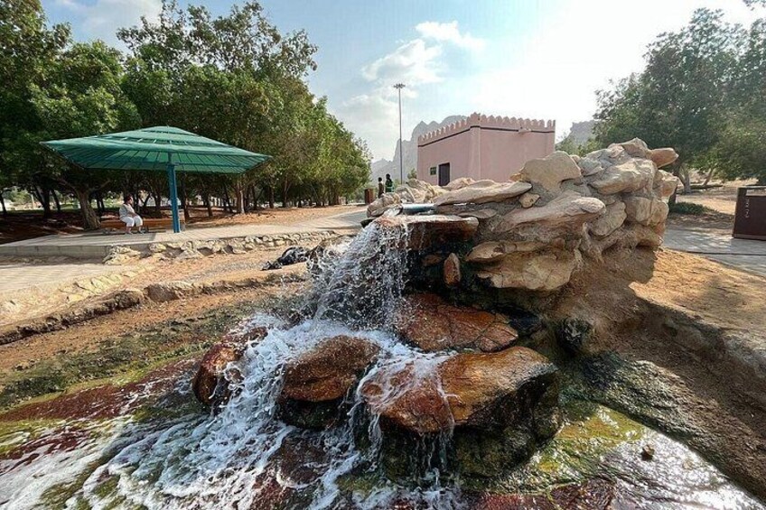 Ein Wasserfall stürzt über Felsen, ein grünes Pavillon und ein Gebäude im Hintergrund. 2