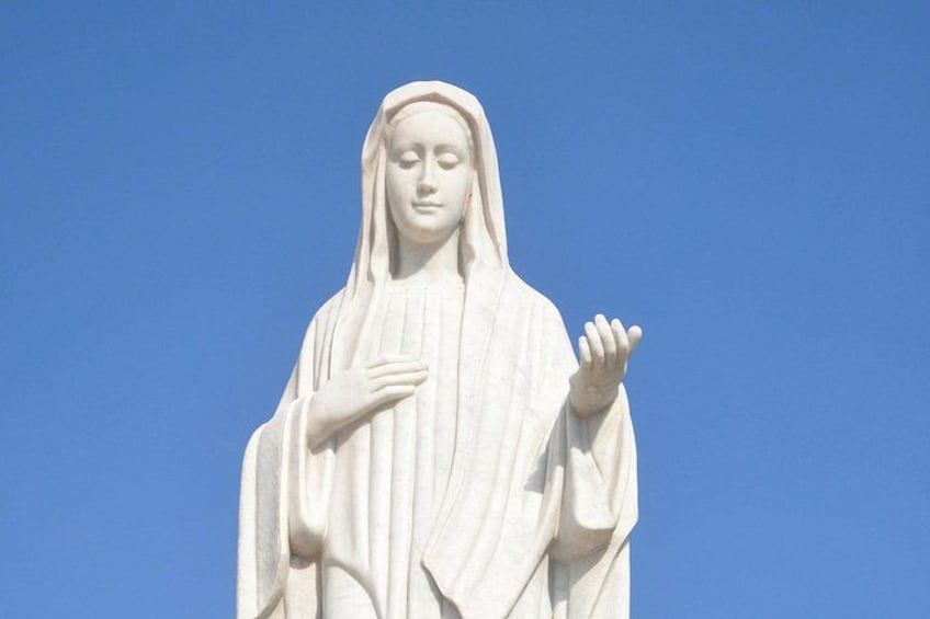 Una estatua de una figura vestida de ropas largas con los brazos extendidos, sobre un cielo azul despejado. 2