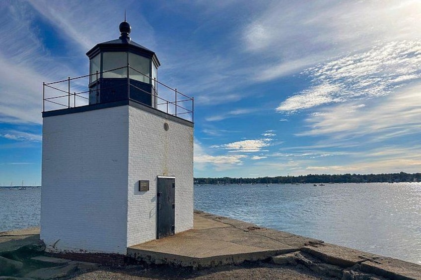 A white lighthouse with a black top, situated on a concrete platform by the water. 2