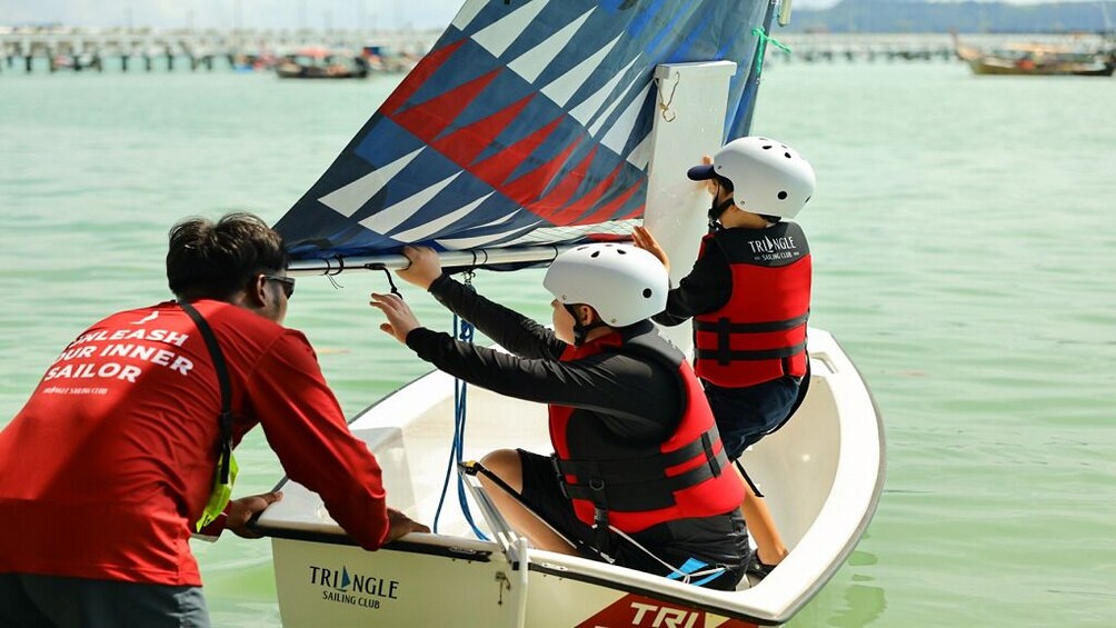 Tres personas en un velero con vela triangular, usando chalecos salvavidas y cascos. 4