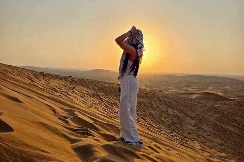 A person standing on a sand dune with the sun setting in the background. 3