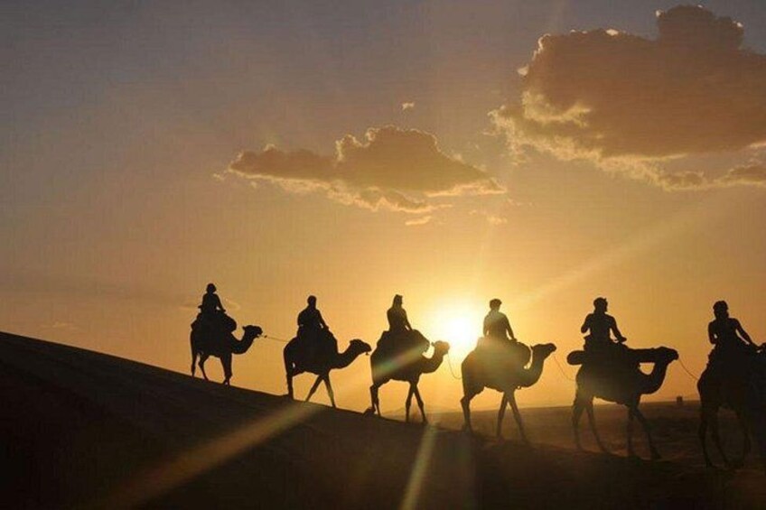 Silhouettes of people riding camels against a sunset. 1