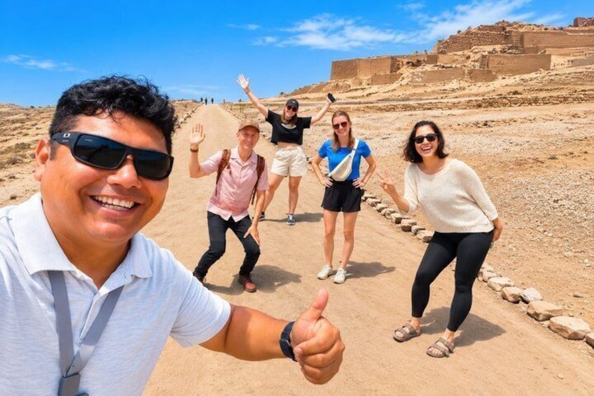 A group of people walking on a sandy path with ancient ruins in the background. 1