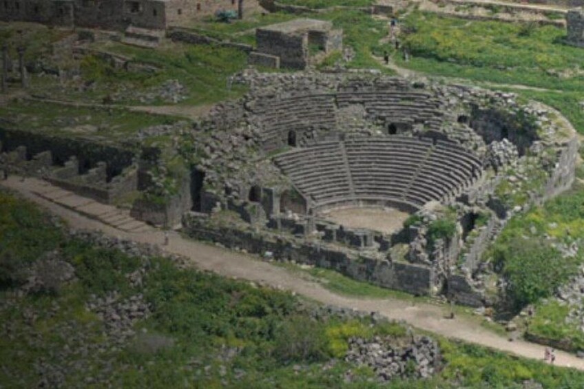 Ein antikes Amphitheater, umgeben von Ruinen und Grünpflanzen. 3