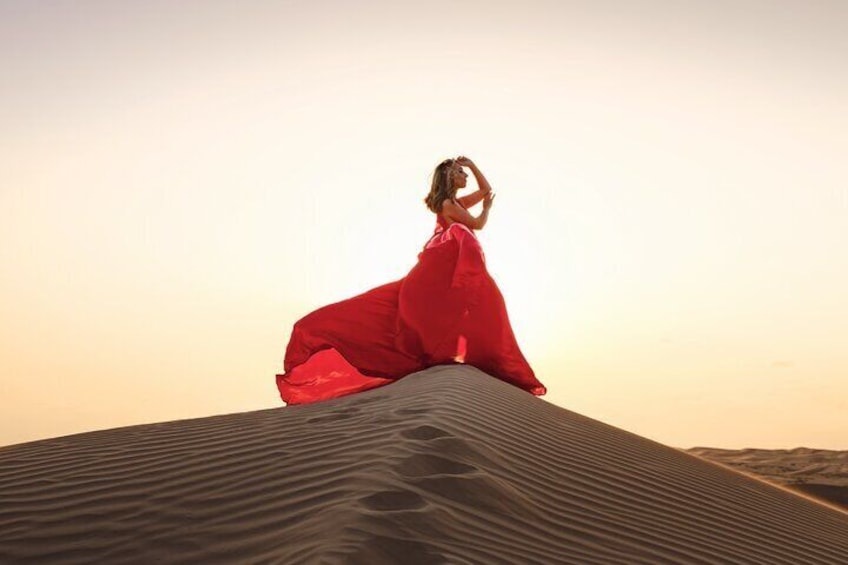 A person in a red dress sitting on a sand dune with a desert landscape in the background. 5