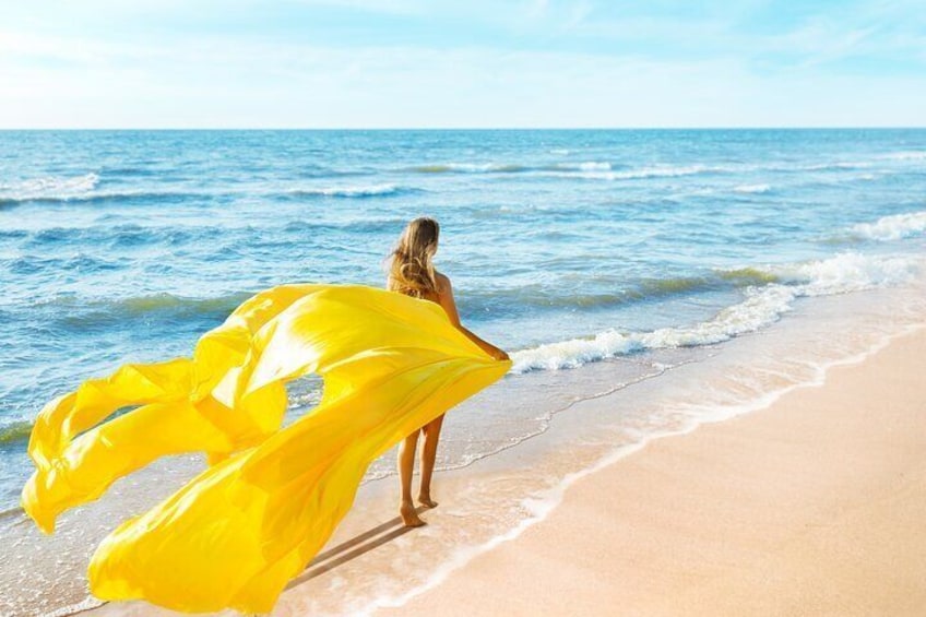 A person standing on a beach holding a yellow fabric. 1