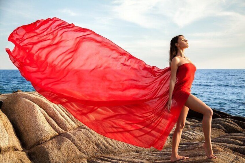 A person in a red dress standing on rocks by the sea. 4