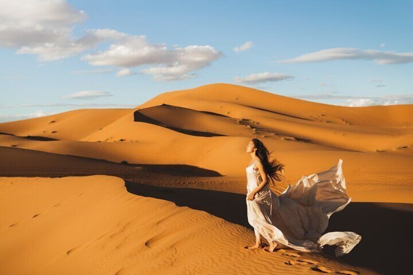 A person in a white dress standing on a sand dune in a desert landscape. 3