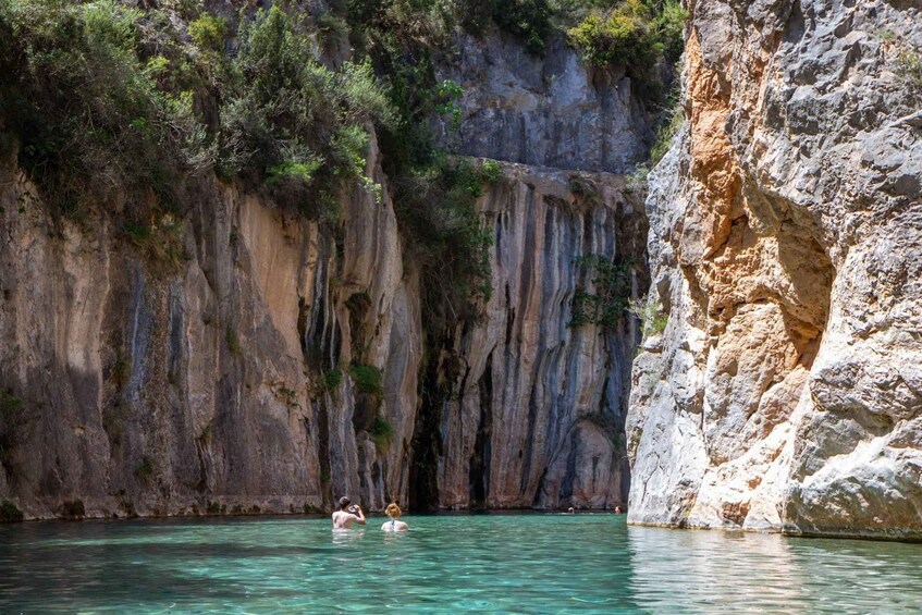 A natural pool surrounded by rocky cliffs with vegetation. 1