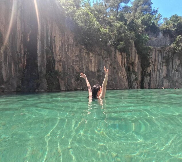 A person swimming in clear water with a rocky cliff in the background. 4