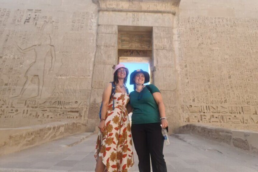 Deux personnes se tiennent devant un ancien mur égyptien orné de hiéroglyphes. 2