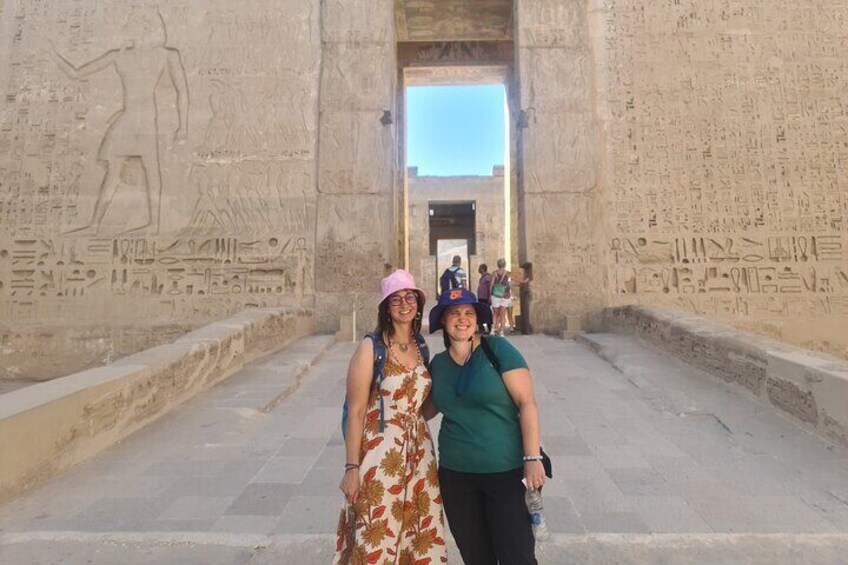 Deux personnes se tiennent devant un ancien mur égyptien orné de hiéroglyphes. 1