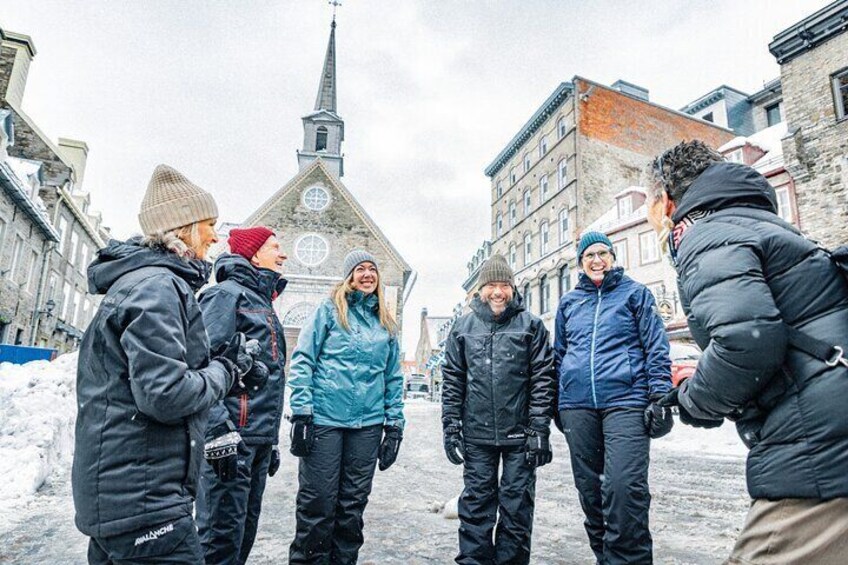 Een groep mensen staat op een besneeuwde stadsstraat met historische gebouwen en een kerk op de achtergrond. 5