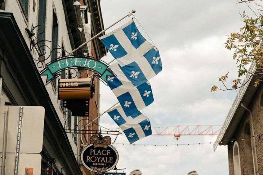 Een gebouw met een bord waarop 'FEEJO' en 'PLACE ROYALE' staan, en blauwe vlaggen met witte kruisen. 3