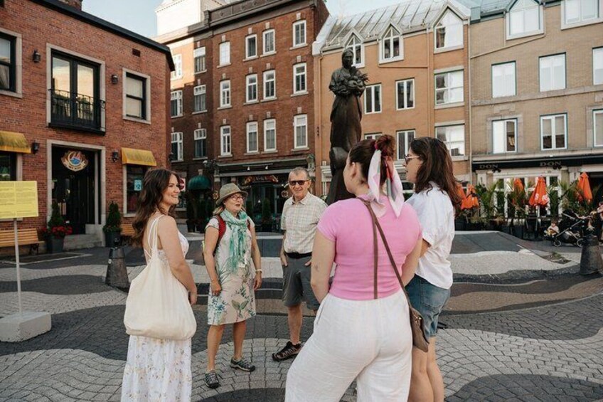 Een groep mensen staat op een openbaar plein, met gebouwen en een standbeeld op de achtergrond. 4