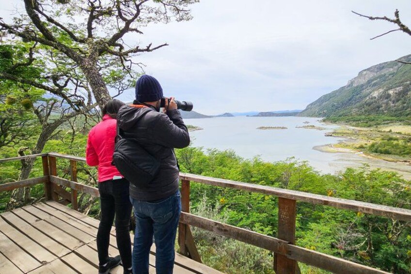 Två personer fotograferar en flod och det omgivande landskapet från en träveranda. 2