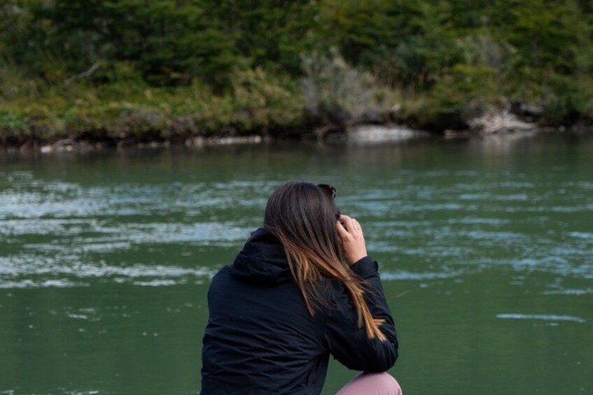 En person sitter vid en flod med grönskande vegetation i bakgrunden. 4