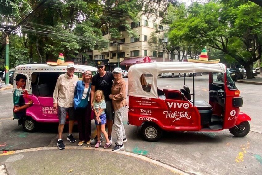 Un grupo de personas de pie frente a un tuk-tuk y un vehículo rosa con la leyenda 'RESALT EL CARS'. 2