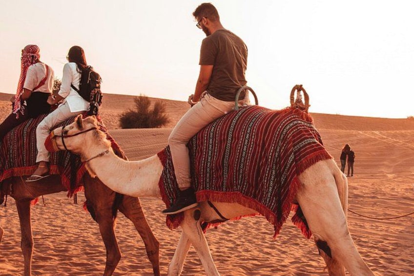 A camel caravan in a desert landscape with people riding camels. 2